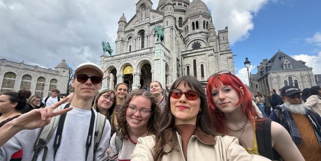 Gruppe junger Menschen vor der Basilika Sacré-Cœur in Paris bei bewölktem Himmel.